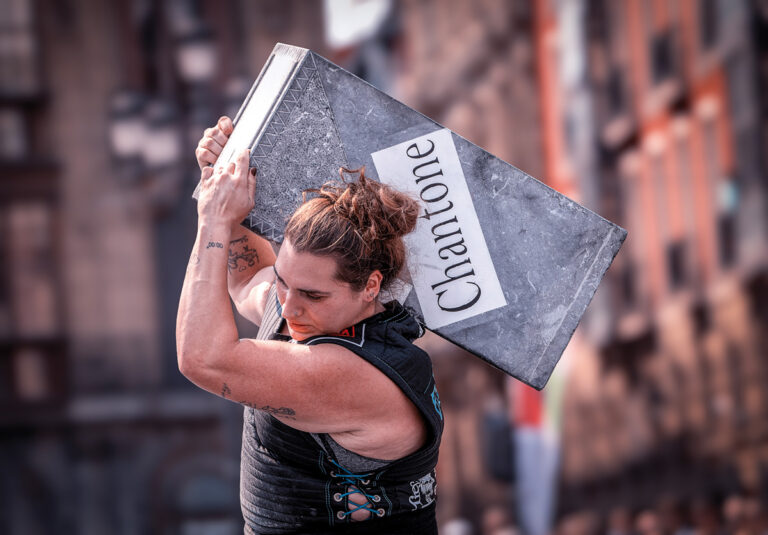 Una harrijasotzaile eleva una piedra rectangular sobre el hombro, símbolo de técnica y potencia.