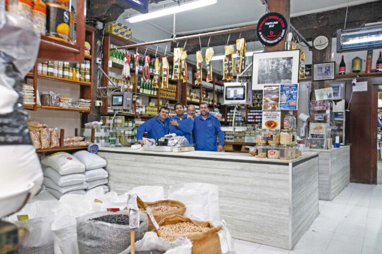 Los trabajadores del ultramarinos, con sus chaquetillas azules, tras el mostrador de mármol y bajo los solivos centenarios. © Hibai Agorria