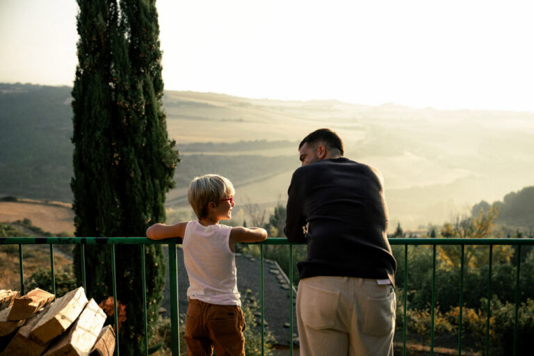 Un adulto y un niño conversan en un balcón con paisaje montañoso al fondo ©Mario Lezaun