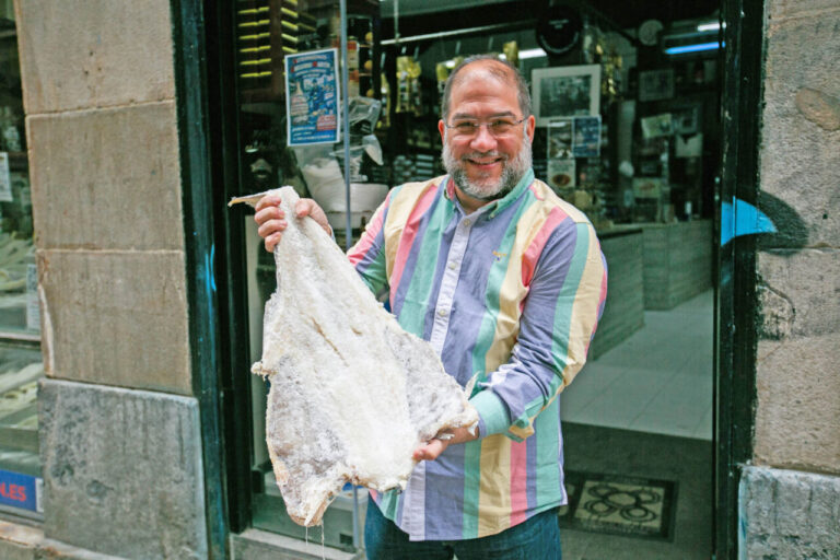 Luis Arbiol Oñate sujeta una bacalada salada en la puerta del colmado antes de cortarla con la guillotina. © Hibai Agorria