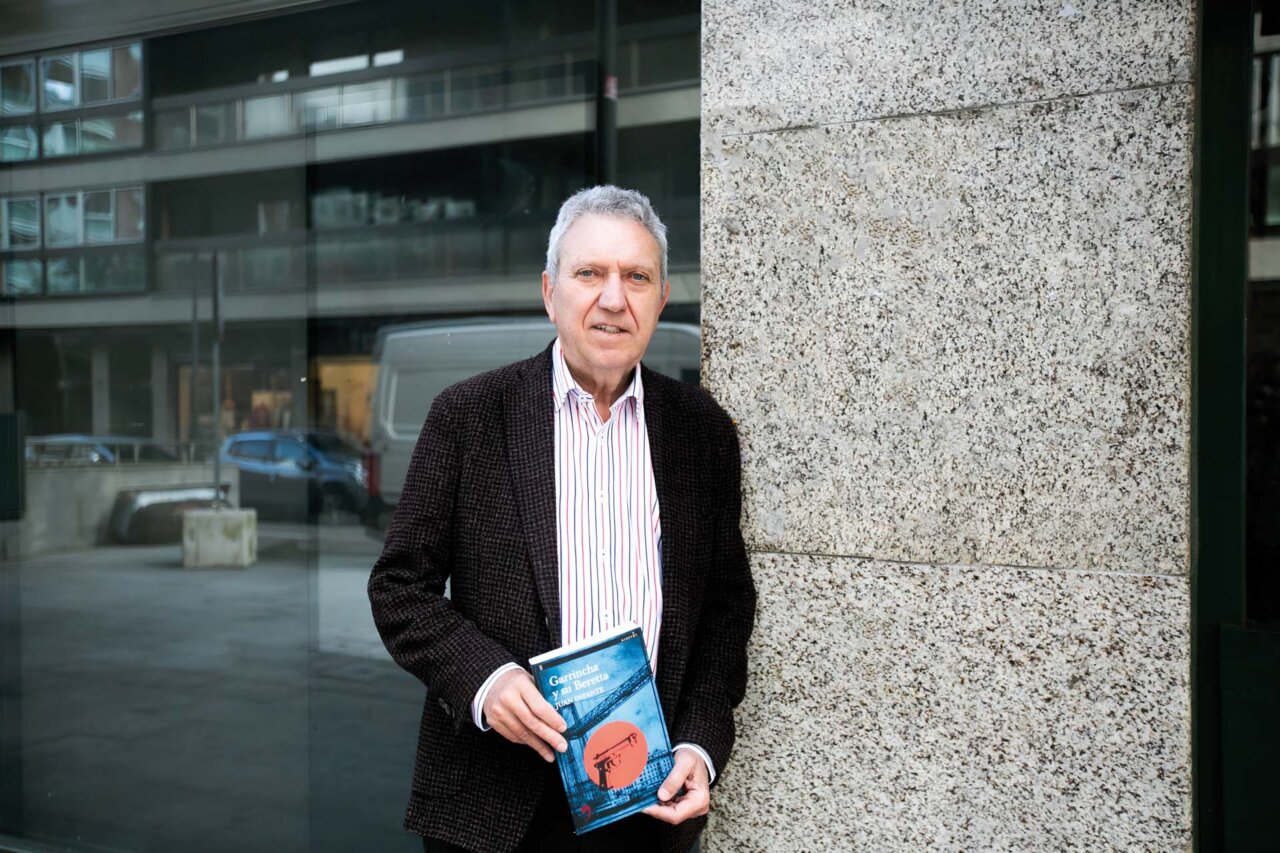 Juan Infante sosteniendo un libro en Bilbao frente a un edificio moderno.